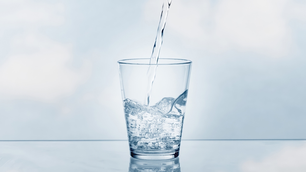 pouring drinking water in a transparent glass isolated on abstract background with glass table, water resource concept with copy space