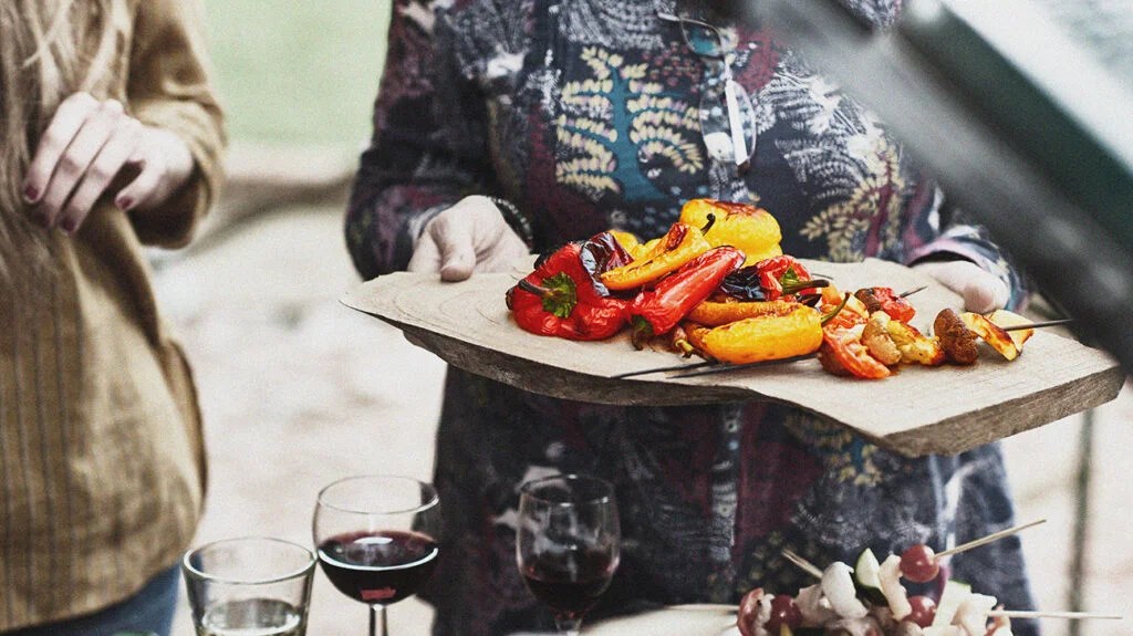 a person carrying a wooden board with grilled peppers
